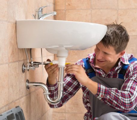 Smiling Male Plumber Repairing Sink — Blocked Drain Services In Runaway Bay, QLD
